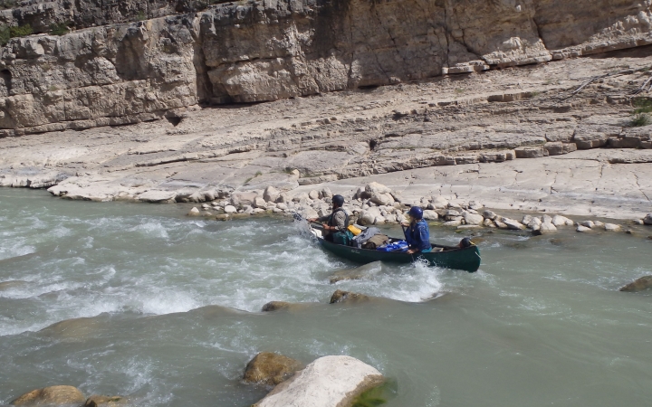 two people in a canoe navigate whitewater on an outward bound veterans trip
